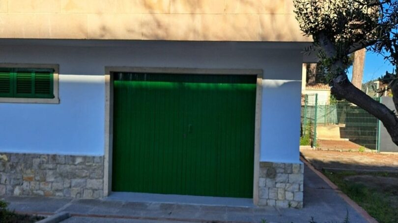 Außenansicht Anwesen Alcúdia: weiße Fassade mit grünen Fensterläden, Garage und Balkon, Olivenbaum im Garten