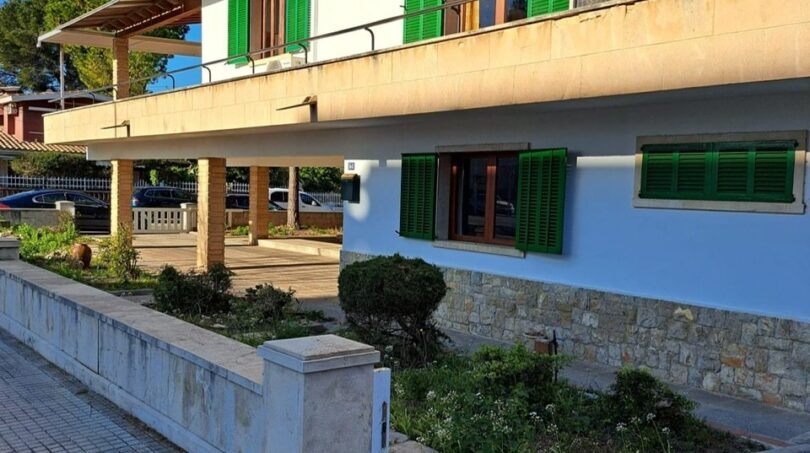 Zweistöckiges Ferienhaus in Alcúdia mit grünen Fensterläden, Balkon, Natursteinverkleidung und gepflegtem Außenbereich.