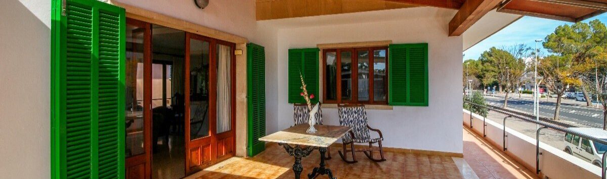 Terraza cubierta con persianas verdes, techo de madera y mesa de bistró, cerca de la playa en Alcudia