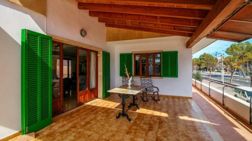 Terraza cubierta con persianas verdes, techo de madera y mesa de bistró, cerca de la playa en Alcudia