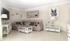 Helles Wohnzimmer des Strandpenthouses mit Chanel-Kissen, weißen Möbeln und stilvollem Kunstwerk in Palma de Mallorca.