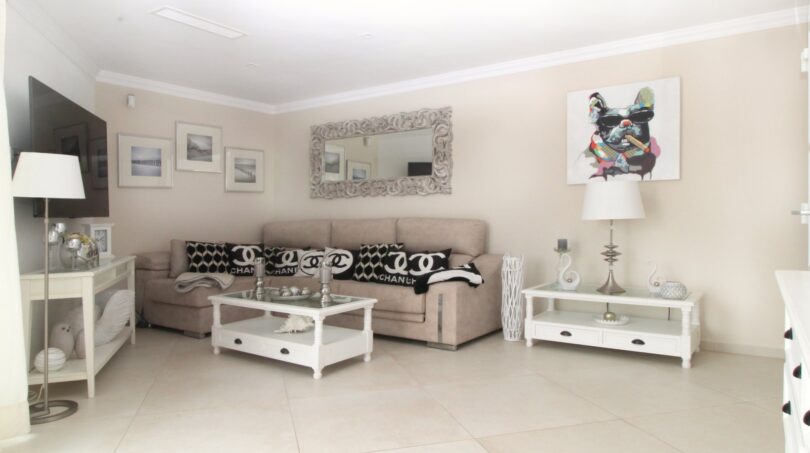 Helles Wohnzimmer des Strandpenthouses mit Chanel-Kissen, weißen Möbeln und stilvollem Kunstwerk in Palma de Mallorca.