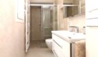 Modernes Badezimmer des Strandpenthouses mit Glasdusche, weißem Waschtisch und Handtuchheizkörper in hellen Beigetönen.