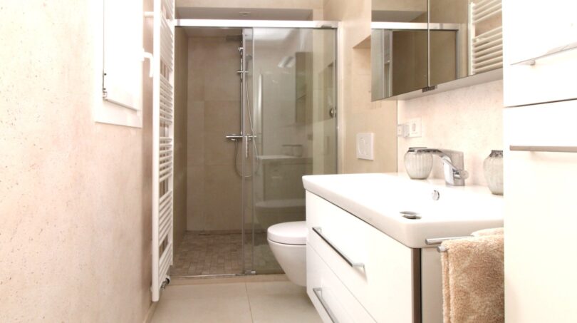 Modernes Badezimmer des Strandpenthouses mit Glasdusche, weißem Waschtisch und Handtuchheizkörper in hellen Beigetönen.