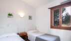 Luminoso dormitorio de la finca Porto Cristo con dos camas individuales, aire acondicionado y ventanas de madera con vista a los árboles.