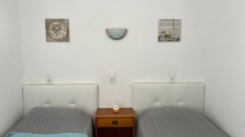 Luminoso dormitorio de la finca en Porto Cristo con dos camas individuales, mesilla y decoración en la pared.