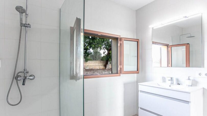 Moderno baño de la finca Porto Cristo con ducha de cristal, doble lavabo y ventanas con vistas a la naturaleza