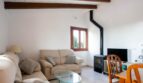 Sala de estar de la finca en Porto Cristo con sofás, techo de vigas de madera, chimenea y ventanas con vistas a la naturaleza.