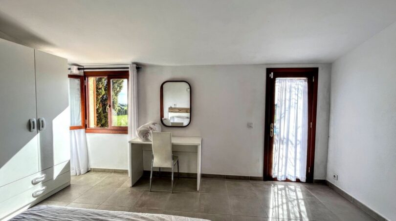 Luminoso dormitorio de la finca en Porto Cristo con escritorio, espejo, acceso al balcón y ventanas con vistas al mar.