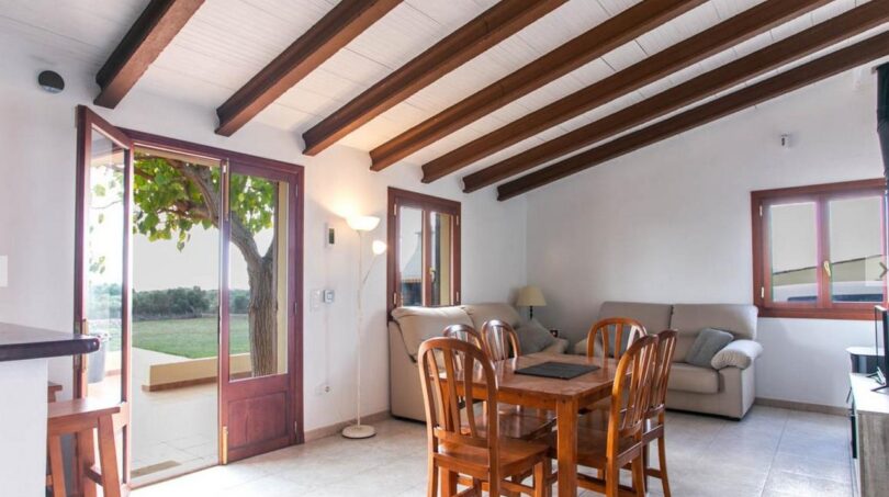 Luminosa sala de estar de la finca con techo de vigas de madera, mesa de comedor y vista al jardín verde.