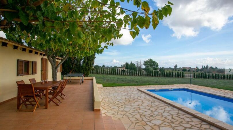 Finca Porto Cristo: Terraza con muebles de madera, piscina y gran jardín bajo árbol frondoso