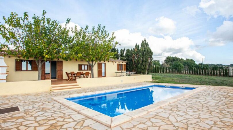 Finca Porto Cristo: Área exterior con piscina azul, suelo de piedra natural y terraza cubierta con conjunto de asientos