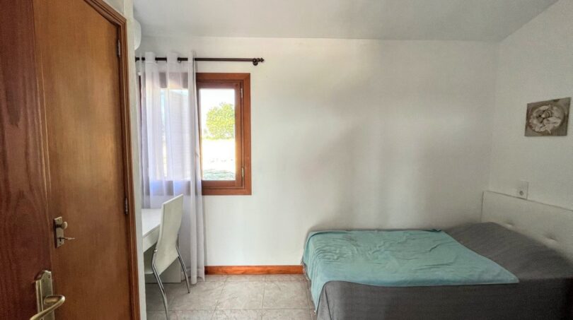 Luminoso dormitorio de la finca en Porto Cristo con cama doble, escritorio y ventanas con vista al jardín.