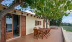 Soleada terraza de la finca Porto Cristo con muebles de madera, zona de barbacoa y árbol que proporciona sombra.