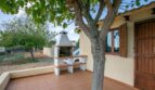 Terraza cubierta de la finca Porto Cristo con barbacoa de piedra, árbol y contraventanas de madera