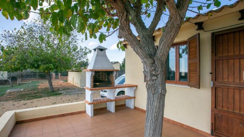 Terraza cubierta de la finca Porto Cristo con barbacoa de piedra, árbol y contraventanas de madera