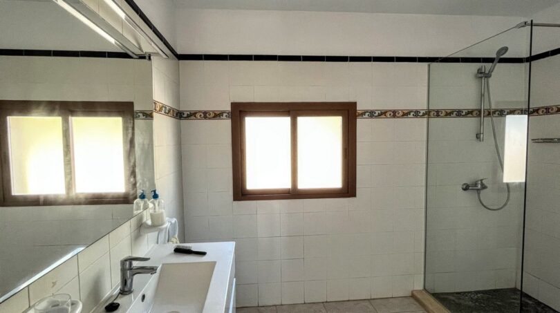 Luminoso baño de la finca en Porto Cristo con ducha de cristal, azulejos blancos y cenefa decorativa