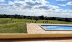 Finca Porto Cristo: Piscina con borde de piedra natural, pradera verde con olivos y amplio panorama bajo cielo azul