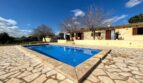 Finca Porto Cristo: Piscina rectangular con terraza de piedra natural y casa de campo mediterránea al fondo.