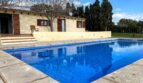 Finca Porto Cristo: Gran piscina exterior rectangular con agua azul, borde de piedra natural y casa de campo mediterránea al fondo.