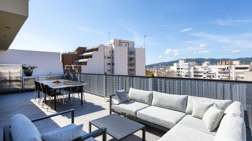 Sonnige Dachterrasse des Luxus-Penthouses in Palma mit Lounge, Esstisch und Stadtpanorama-Blick.