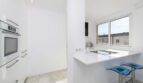 Moderne weiße Küche im Luxus-Penthouse Palma mit Kochblock, Einbaugeräten und blauen Barhockern.