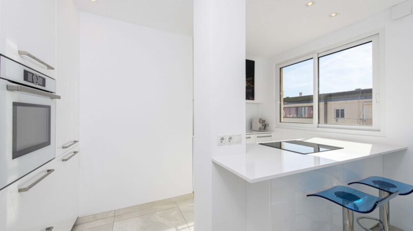 Moderne weiße Küche im Luxus-Penthouse Palma mit Kochblock, Einbaugeräten und blauen Barhockern.