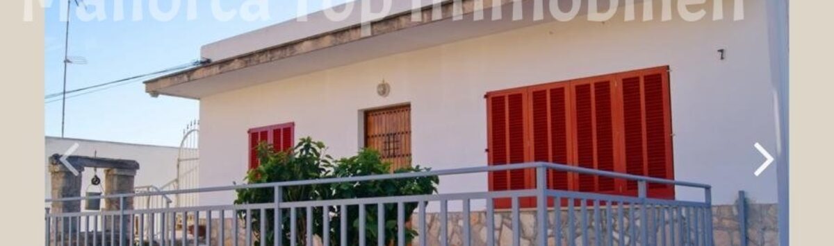 Außenansicht Zweifamilienhaus Portocolom: weißes Gebäude mit roten Fensterläden, Balkon und Metallgeländer.