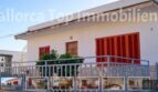 Außenansicht Zweifamilienhaus Portocolom: weißes Gebäude mit roten Fensterläden, Balkon und Metallgeländer.