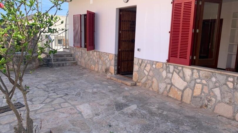 Außenbereich eines Zweifamilienhauses in Portocolom mit Natursteintetrasse, roter Holztür und Fensterläden.