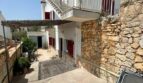 Außenbereich des Zweifamilienhauses in Portocolom mit Balkon, roten Fensterläden und mediterraner Natursteinmauer.