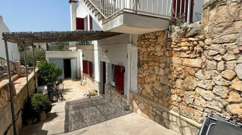 Außenbereich des Zweifamilienhauses in Portocolom mit Balkon, roten Fensterläden und mediterraner Natursteinmauer.