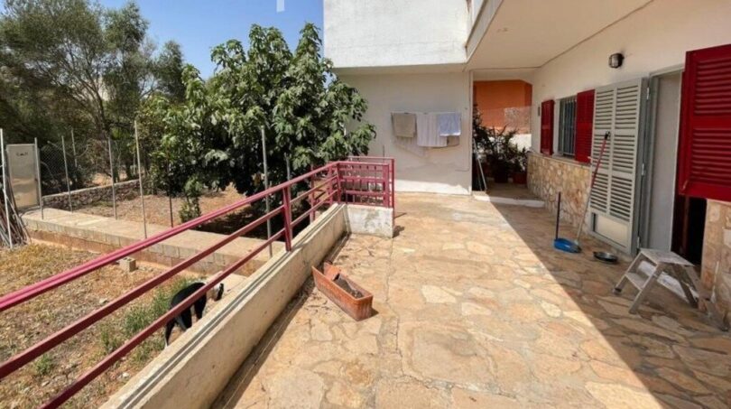 Terrasse mit Natursteinboden, rotem Geländer und Gartenblick des Zweifamilienhauses in Portocolom