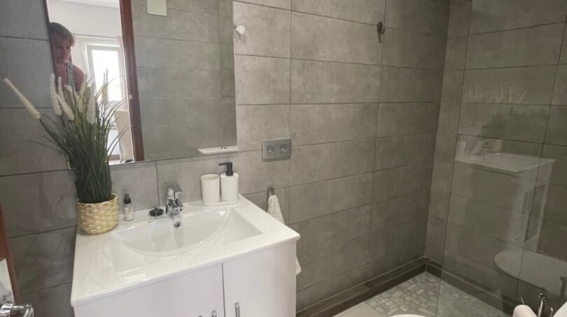 Modernes Badezimmer mit grauer Fliesenoptik, weißem Waschtisch, Dusche und WC im Zweifamilienhaus Portocolom
