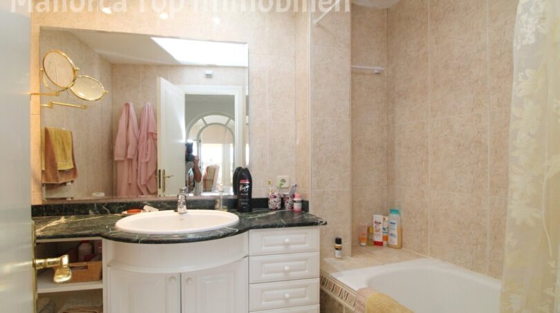 Elegantes Badezimmer mit Marmor-Waschtisch, weißem Unterschrank, Badewanne und beigen Fliesen in Mallorca-Wohnung