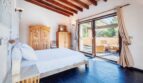 Dormitorio luminoso de la villa en Calvia con techo de vigas de madera, cama doble y acceso a terraza con zona de estar