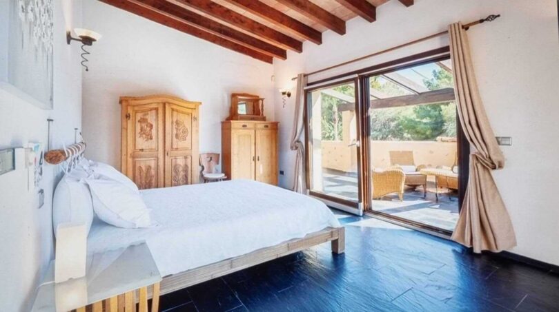Dormitorio luminoso de la villa en Calvia con techo de vigas de madera, cama doble y acceso a terraza con zona de estar