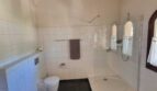 Baño luminoso de la villa con azulejos blancos, ducha, WC, bidé y vigas de madera rústicas en el techo.