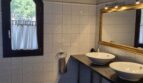 Elegante baño de la villa con dos lavabos sobre encimera, espejo dorado y ventana de arco redondo