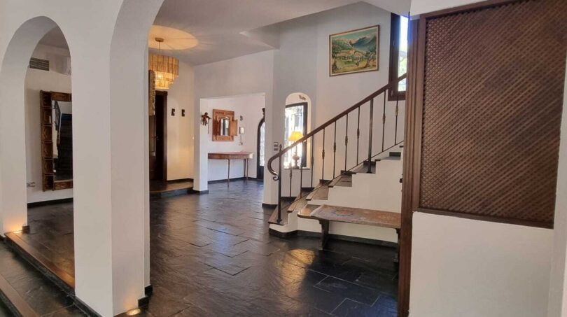 Zona de entrada de la villa en Calvia con arcos redondos, suelo de piedra natural oscura y elegante escalera.
