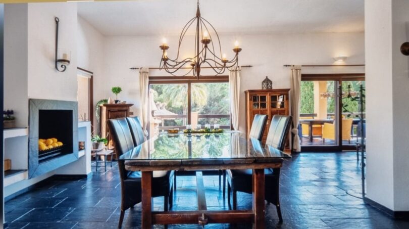 Elegante comedor de la villa en Calvia con mesa de cristal, chimenea y vistas al jardín mediterráneo