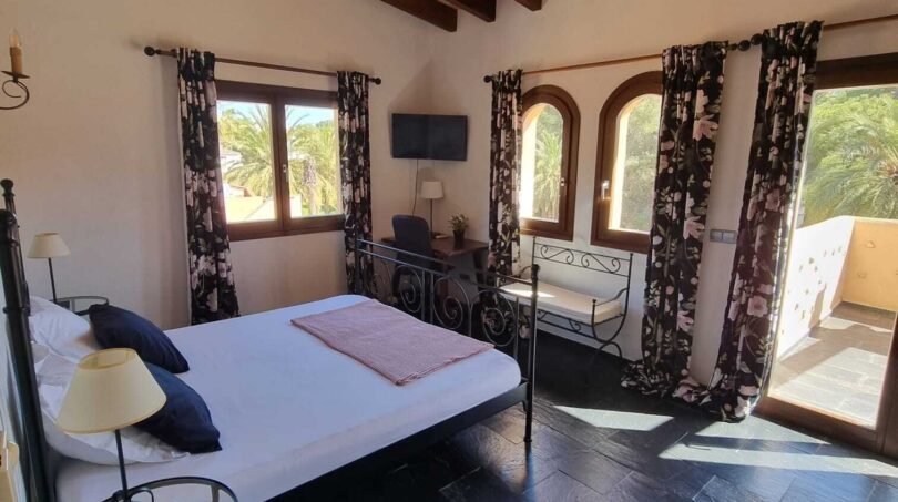 Dormitorio luminoso con techo de vigas de madera, cama de hierro forjado y vistas a las palmeras en villa exclusiva, Calvia