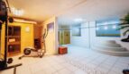 Área de bienestar de la villa con sauna, elíptica, jacuzzi y zona de ducha con decoración de pared azul.