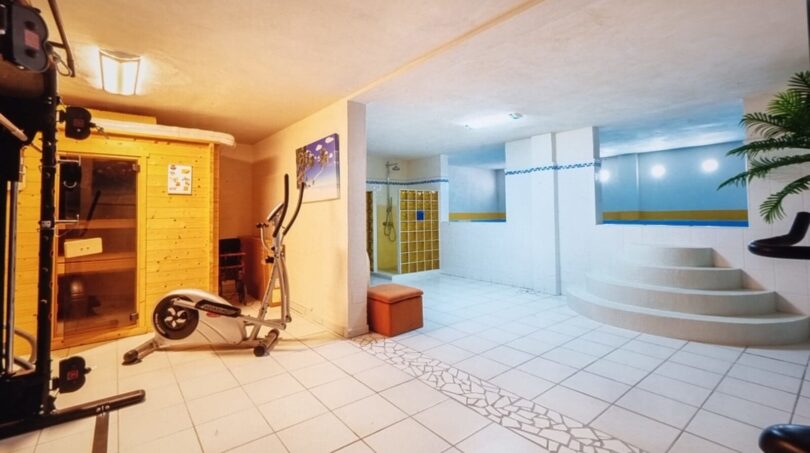 Área de bienestar de la villa con sauna, elíptica, jacuzzi y zona de ducha con decoración de pared azul.