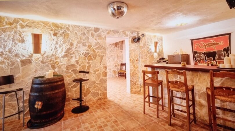 Rústica barra en el sótano de la villa con muros de piedra natural, mostrador de madera, tonel de vino y bola de discoteca en Calvia