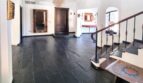 Zona de entrada de la villa con suelo de piedra natural oscura, escalera de madera, araña y elegante portal de madera.