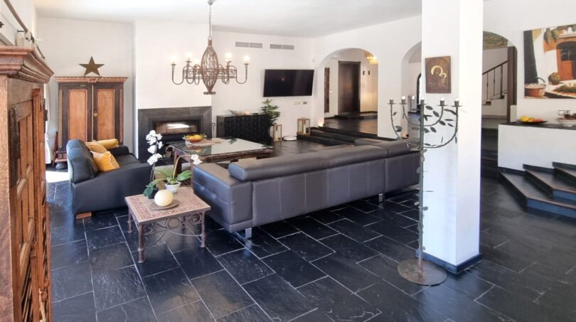 Amplio salón de la villa en Calvia con suelo de piedra natural negra, sofá de cuero y elegante araña.