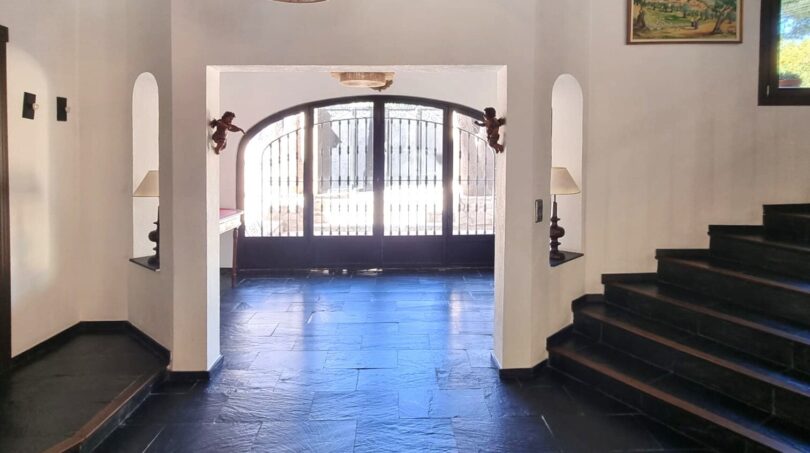 Elegante zona de entrada de la villa con suelo de pizarra negra, puerta de arco redondo y escalera en Calvia.