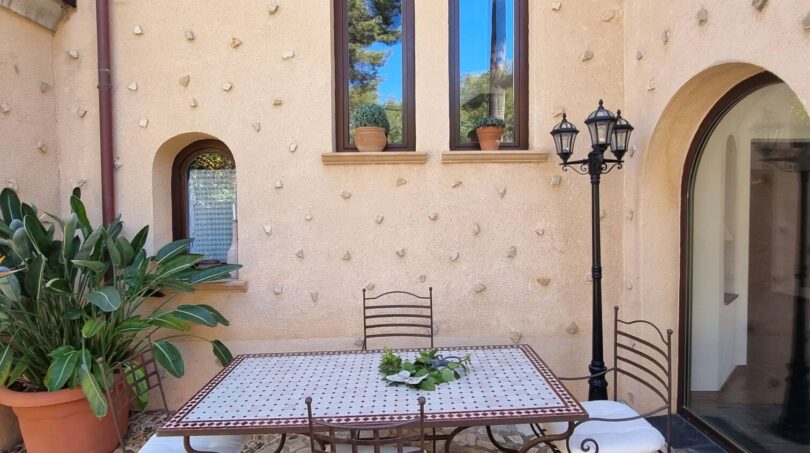 Patio interior mediterráneo de la villa en Calvia con mesa de mosaico, sillas de hierro forjado y muro de piedra natural rústica