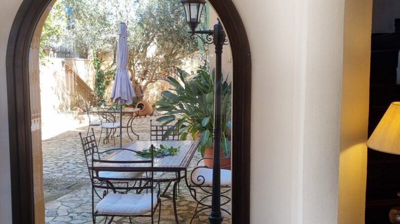 Paso abovedado con vistas al patio interior mediterráneo con muebles de hierro, suelo de piedra y olivo de la villa en Calvia
